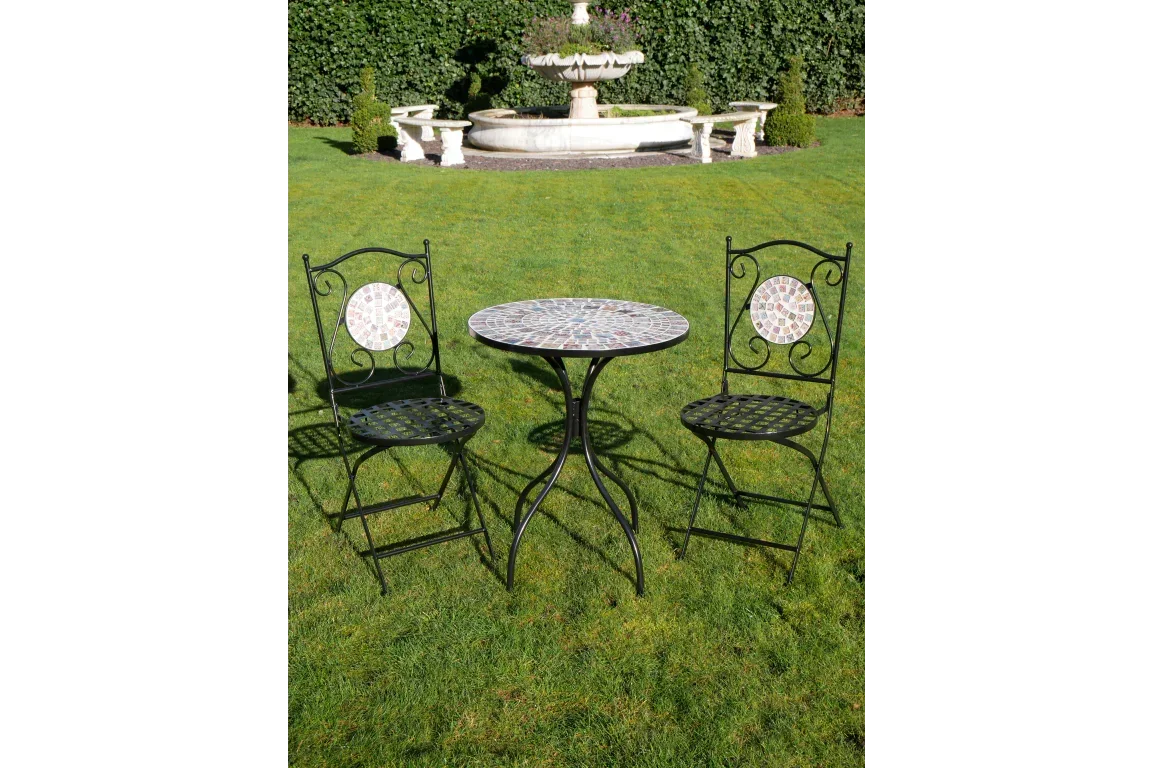 Mosaic bistro table and two metal chairs on lawn with garden fountain in background
