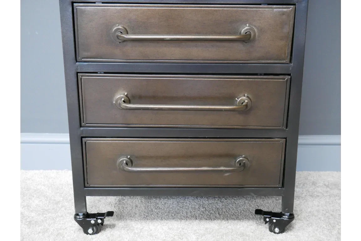 Industrial metal chest of drawers with three bronze handles and castor wheels on carpet