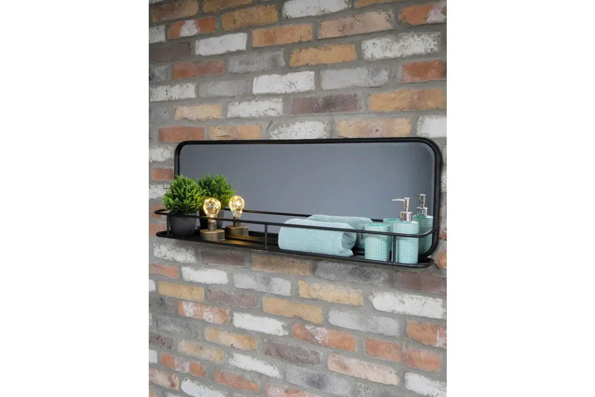 Rectangular wall mirror with black shelf holding towels, soap dispensers, and decor