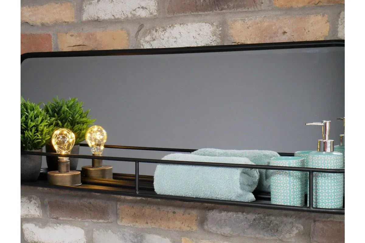 Rectangular wall mirror with shelf holding LED bulbs, green towel, plant, and ceramic dispensers