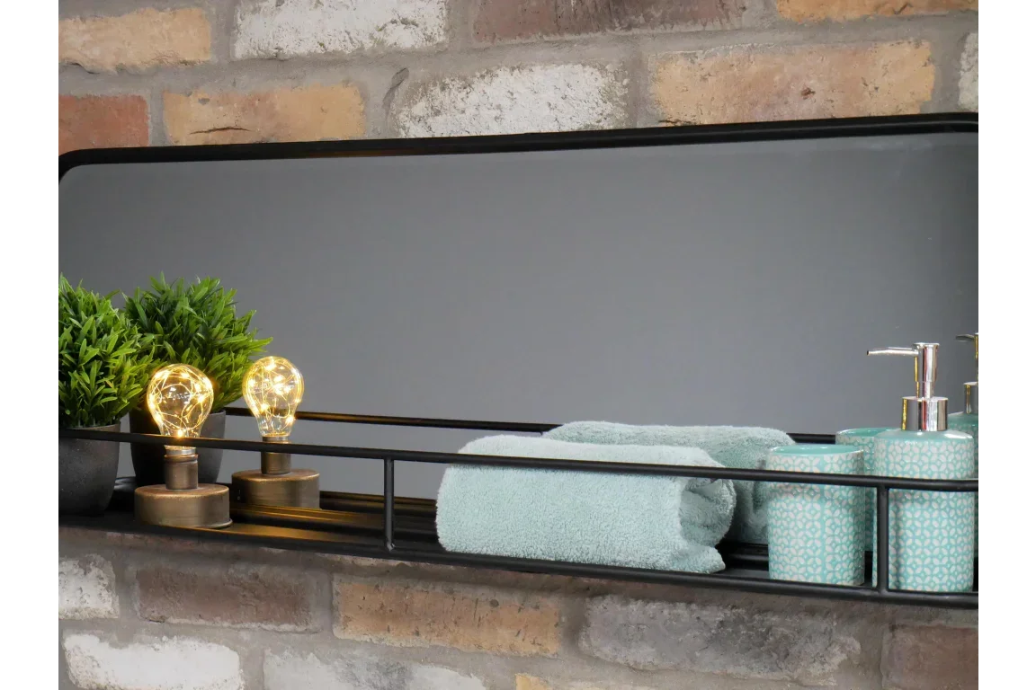 Rectangular bathroom mirror with shelf holding teal towel, soap dispensers and decorative bulbs