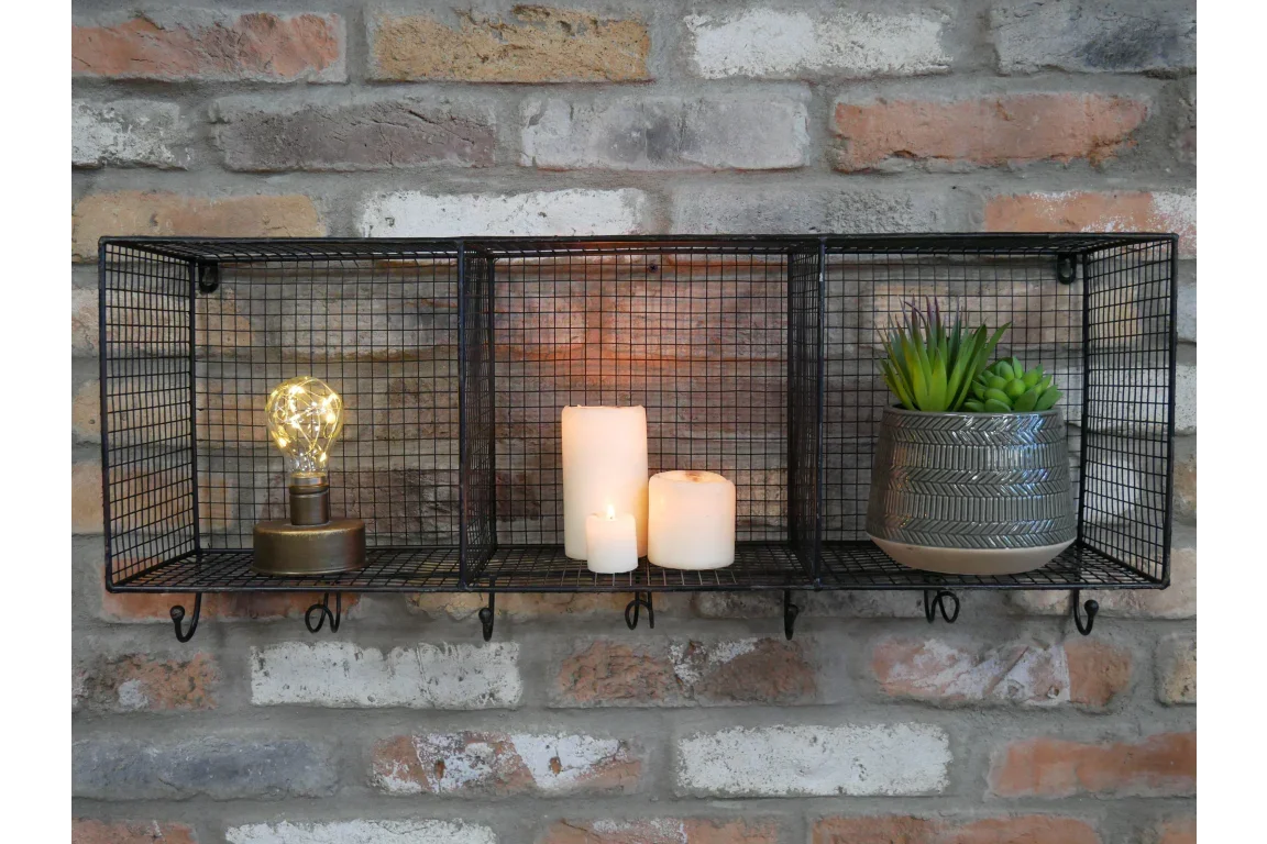 Black wire wall shelf with hooks, candles, small lamp, and artificial green plant