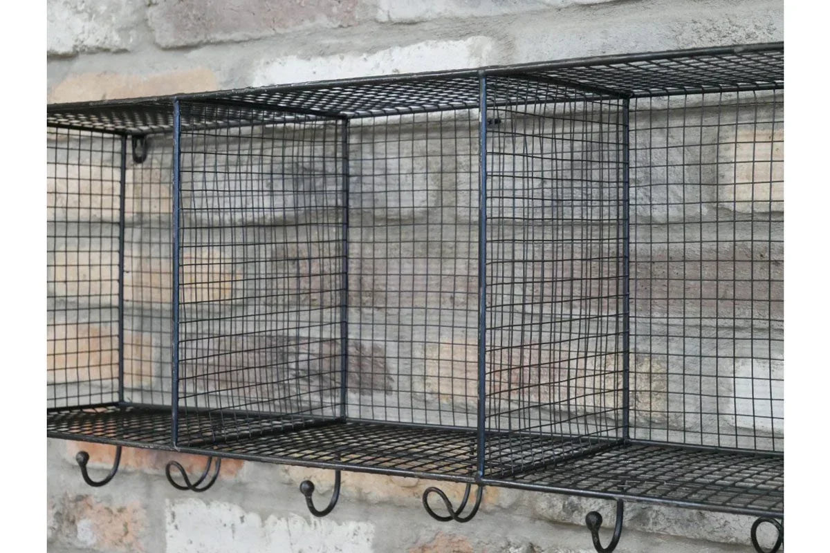 Black wire wall shelf with cubby compartments and hooks against a brick wall