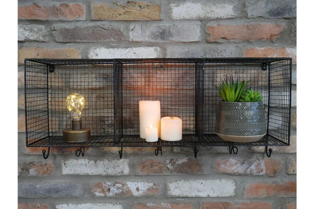 Black metal wall shelf with hooks, decorated with candles, lamp, and potted succulent plant