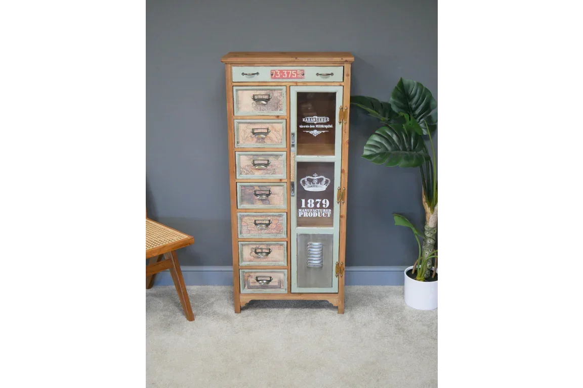 Tall wooden cabinet with seven drawers and one glass door, vintage print details, against grey wall