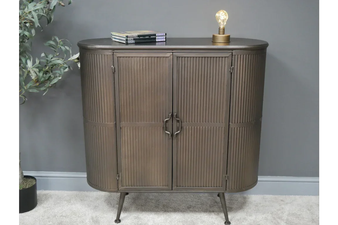 Bronze metal sideboard cabinet with ribbed doors and slim legs, styled with books and lamp