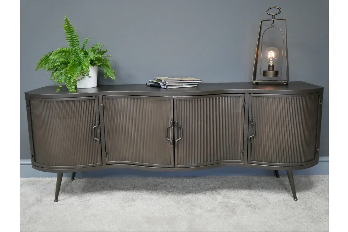 Black metal sideboard with ribbed doors, plant, magazines, and table lamp on grey carpet