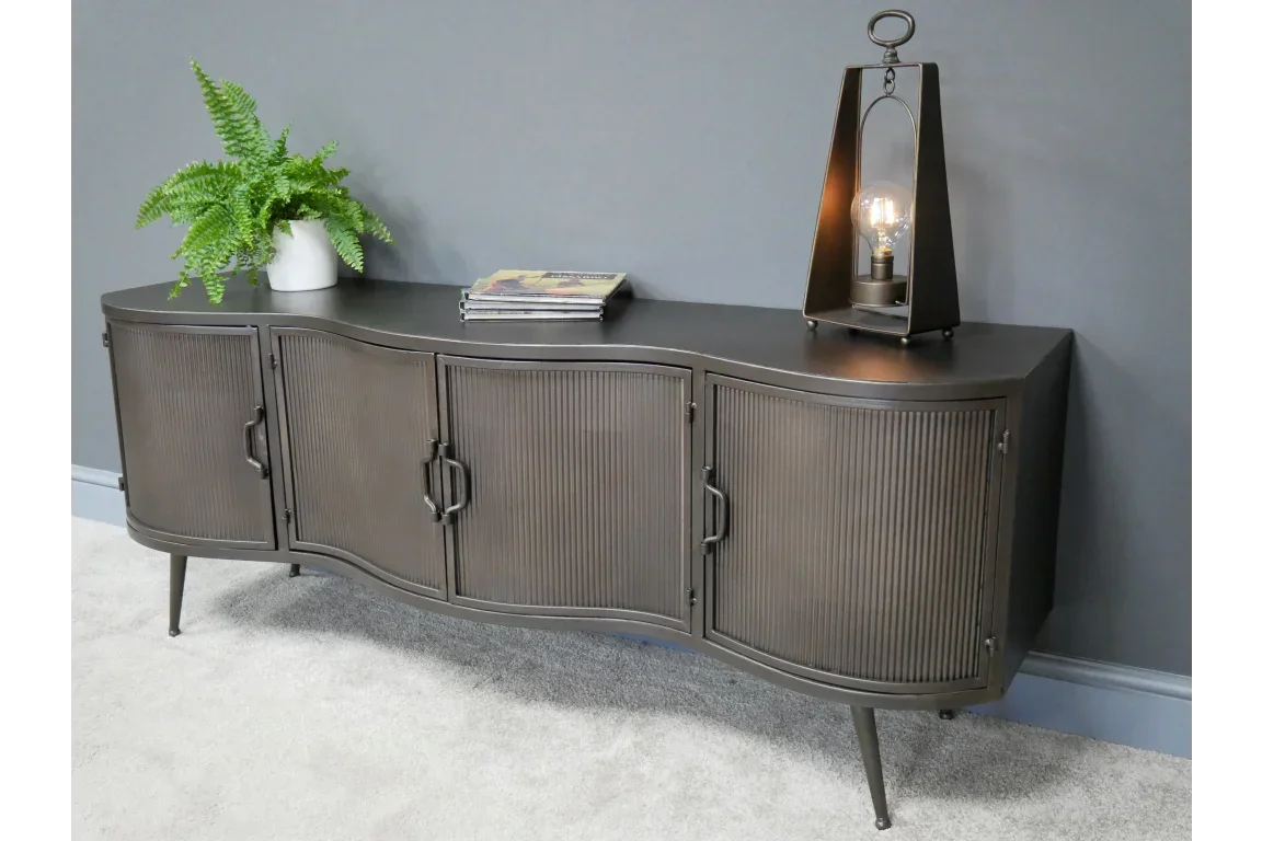 Black ribbed metal sideboard with curved doors on legs, styled with a plant and lamp