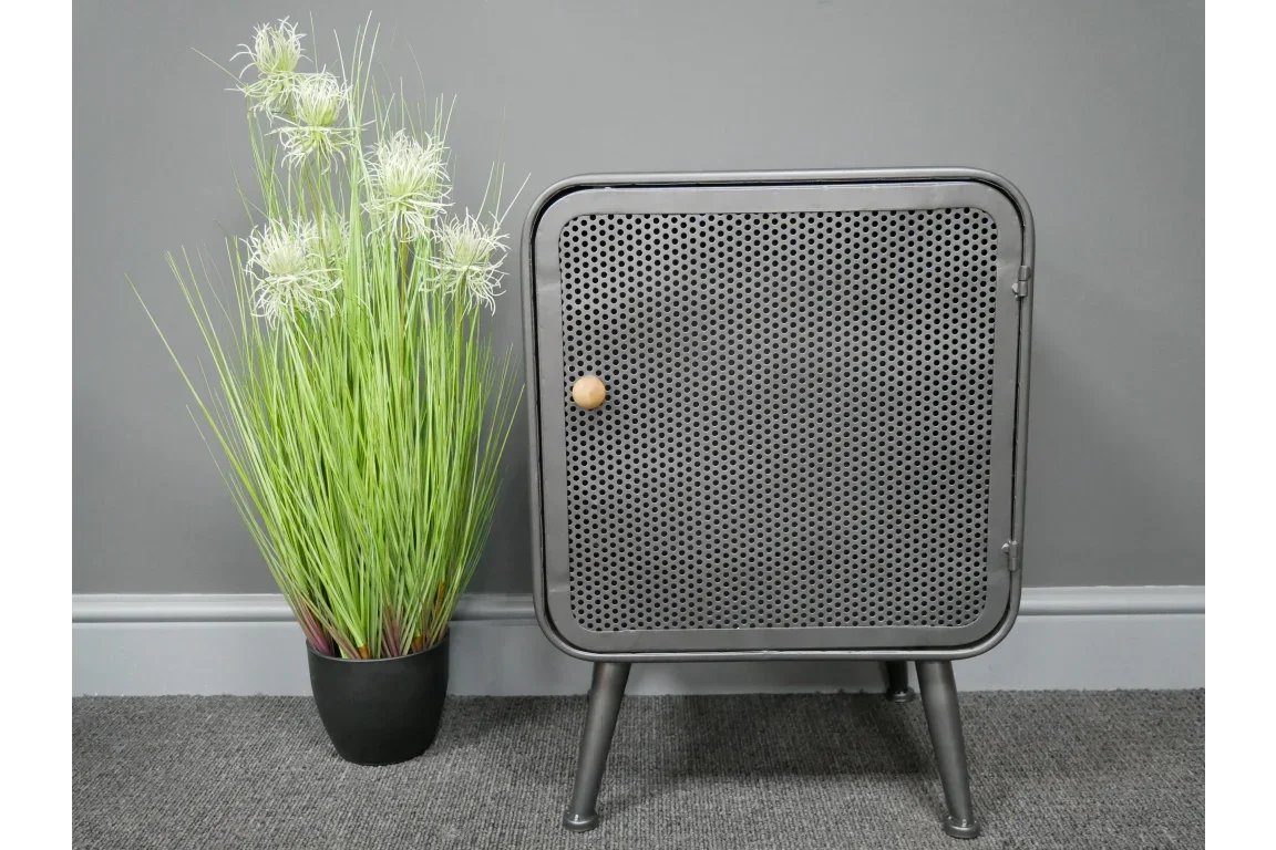 Industrial metal side cabinet with perforated door beside tall green artificial plant