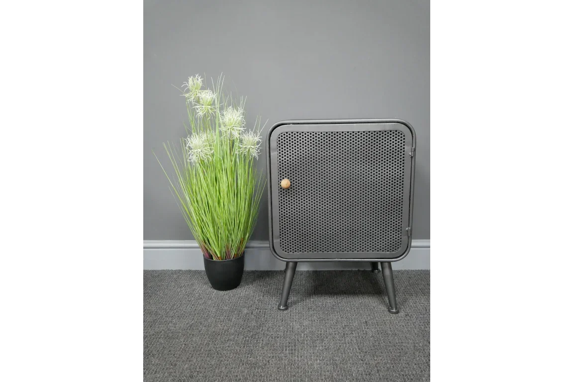 Black metal storage cabinet with mesh door beside artificial grass plant on grey carpet