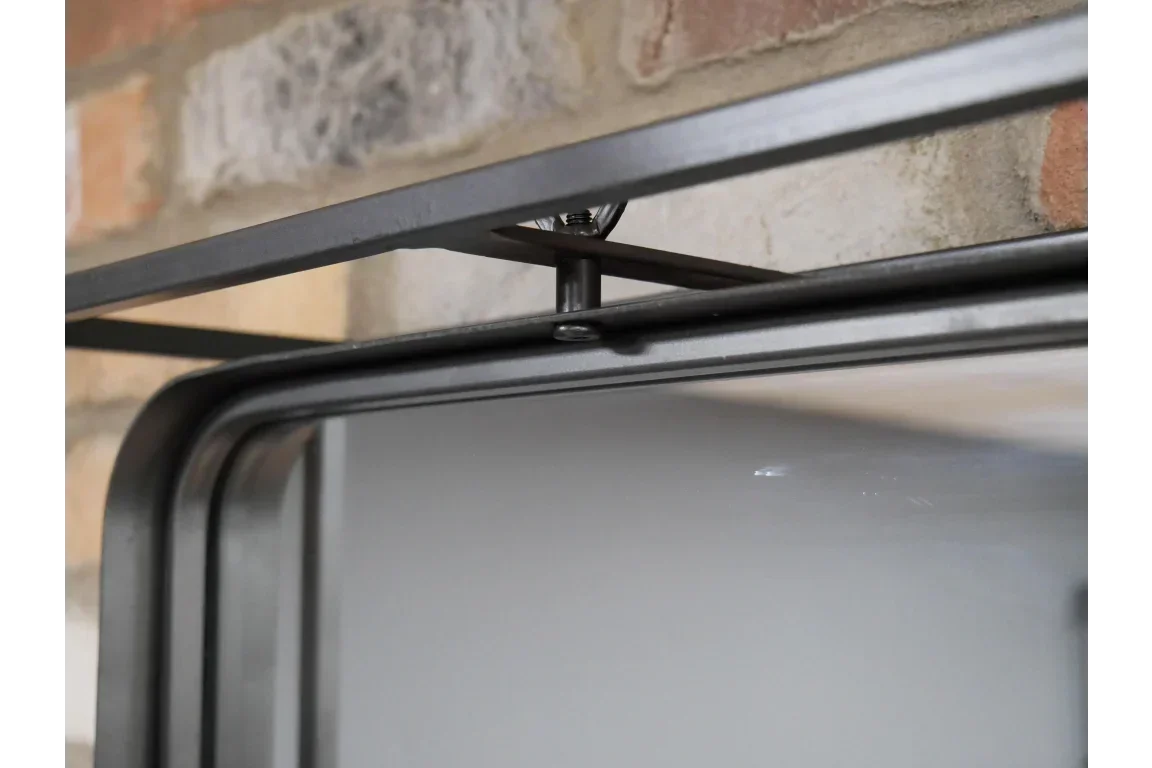 Black metal frame wall mirror close-up with industrial bolt detail against brick wall
