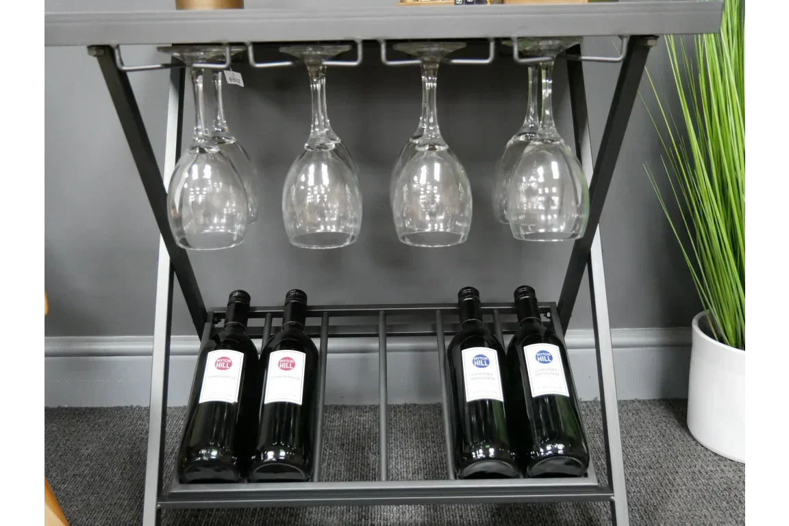 Metal wine rack with four hanging wine glasses and four bottles on lower shelf