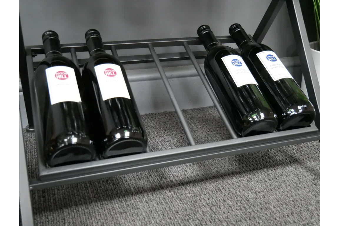 Black metal wine rack with four wine bottles on grey carpeted floor