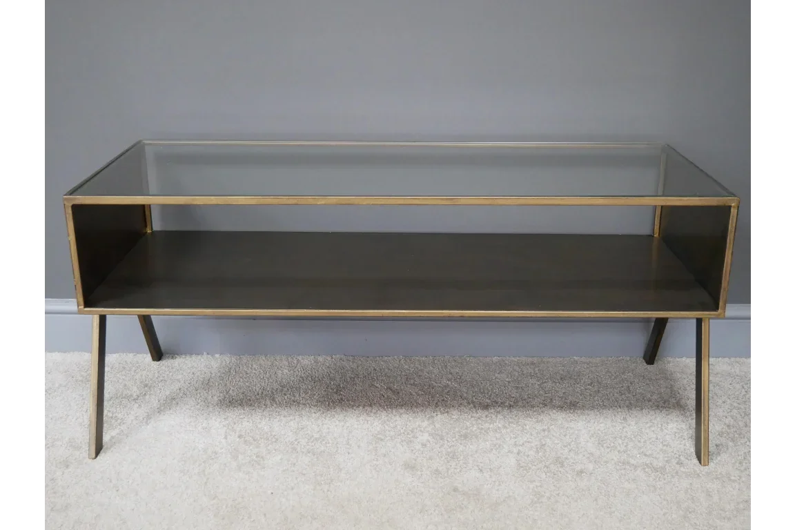 Glass top coffee table with gold metal frame and open shelf on neutral carpet