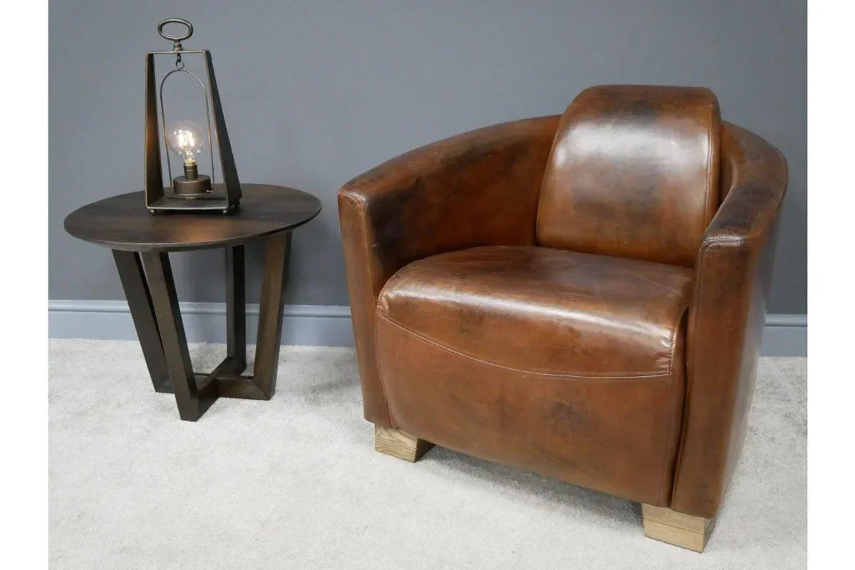 Brown leather armchair beside modern round side table with lamp on light carpet