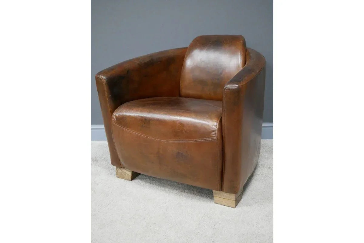 Brown leather armchair with curved arms and wooden legs against grey wall