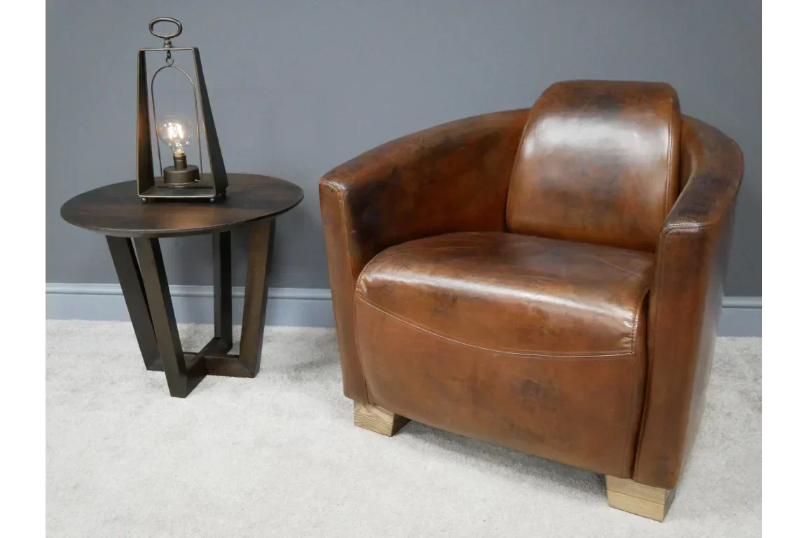 Brown leather armchair with wooden legs next to a round side table and modern lamp