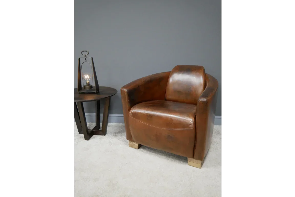 Brown leather armchair with wooden legs beside a round side table and decorative lamp