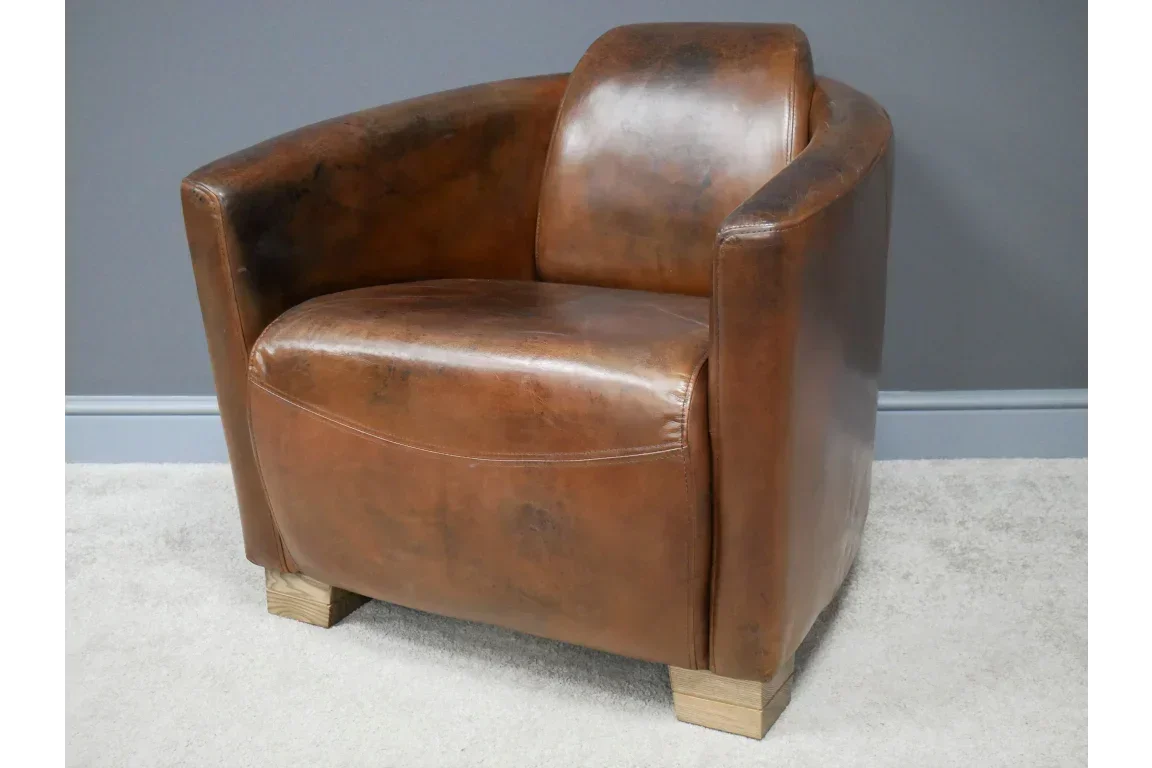 Brown leather armchair with curved backrest and wooden block legs on a light carpet
