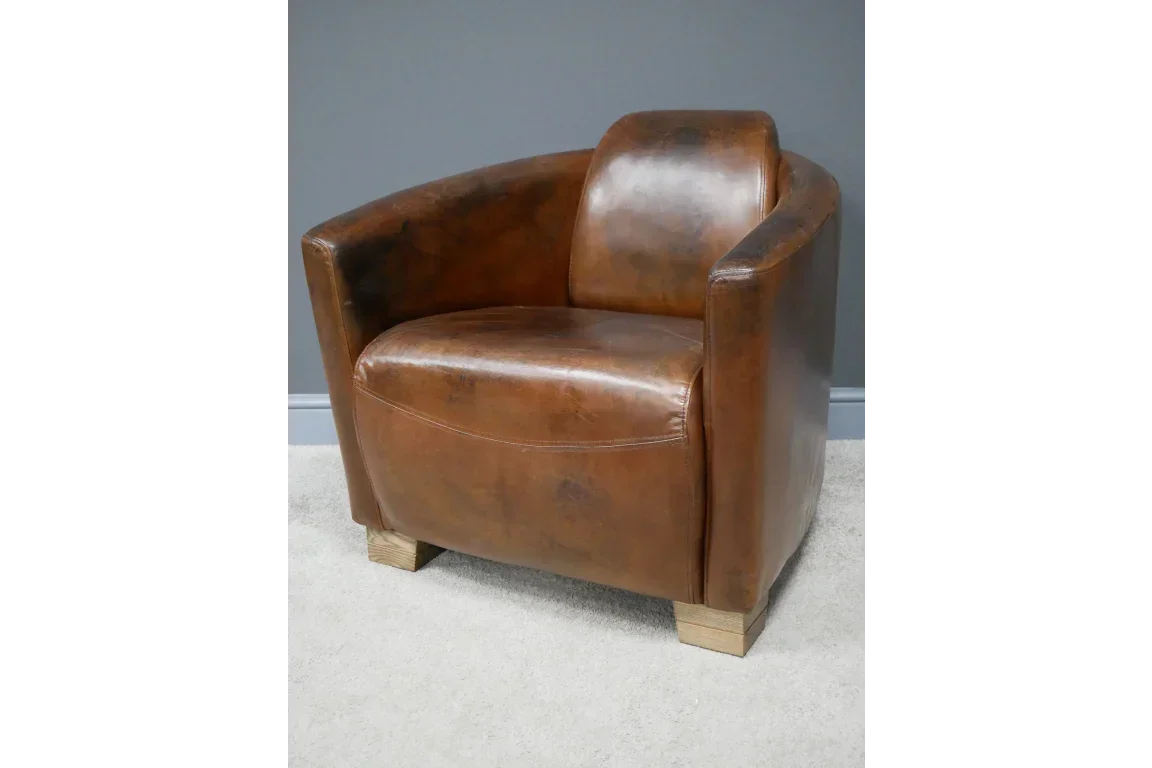Brown leather armchair with curved backrest and wooden legs on light carpet