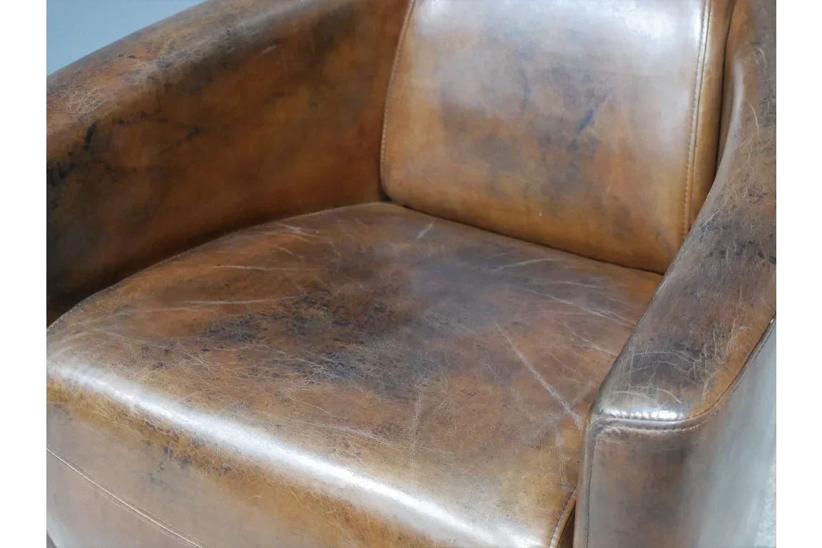 Distressed brown leather armchair close-up showing seat, armrest, and stitching detail