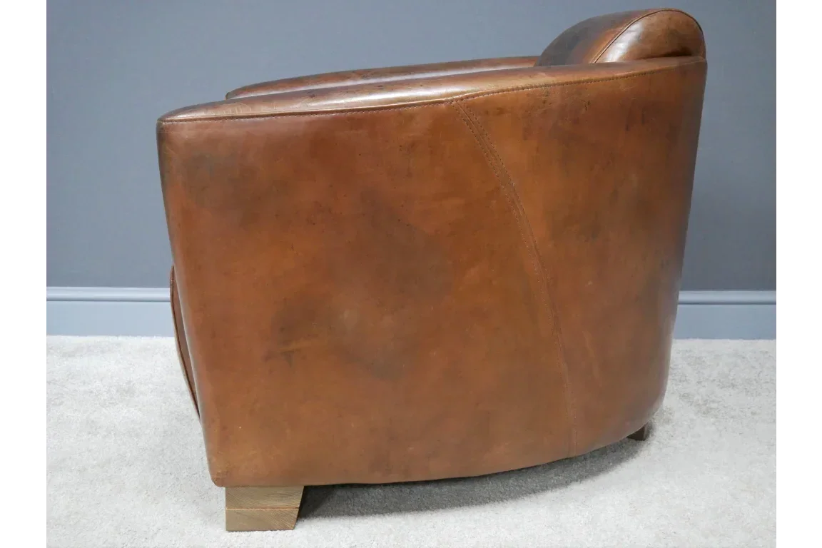 Side view of brown leather armchair with wooden feet on light carpet
