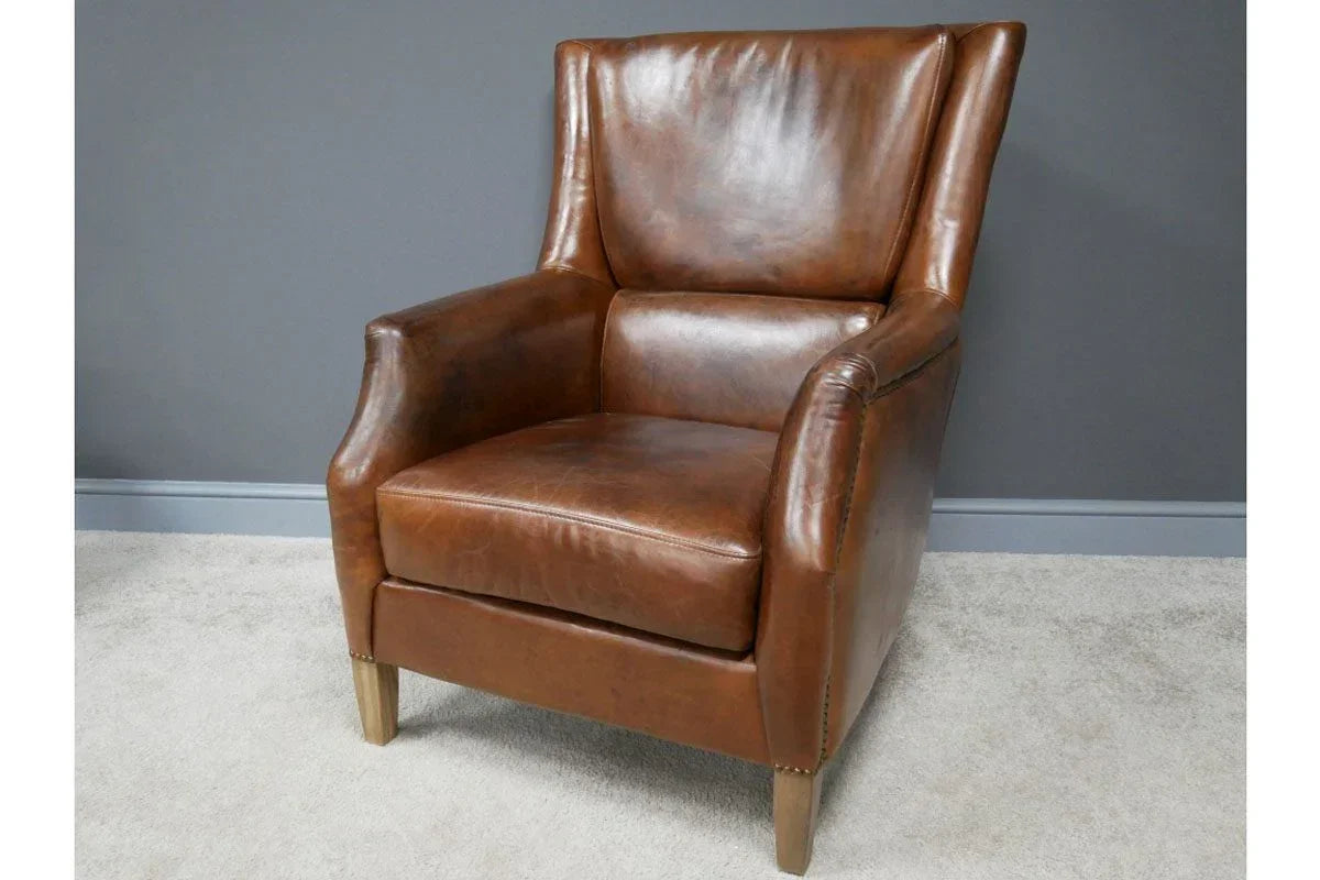 Brown leather armchair with wooden legs against grey wall on light carpet