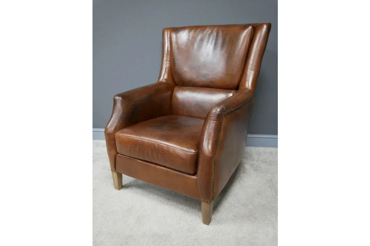 Brown leather armchair with wooden legs against grey wall on light carpet
