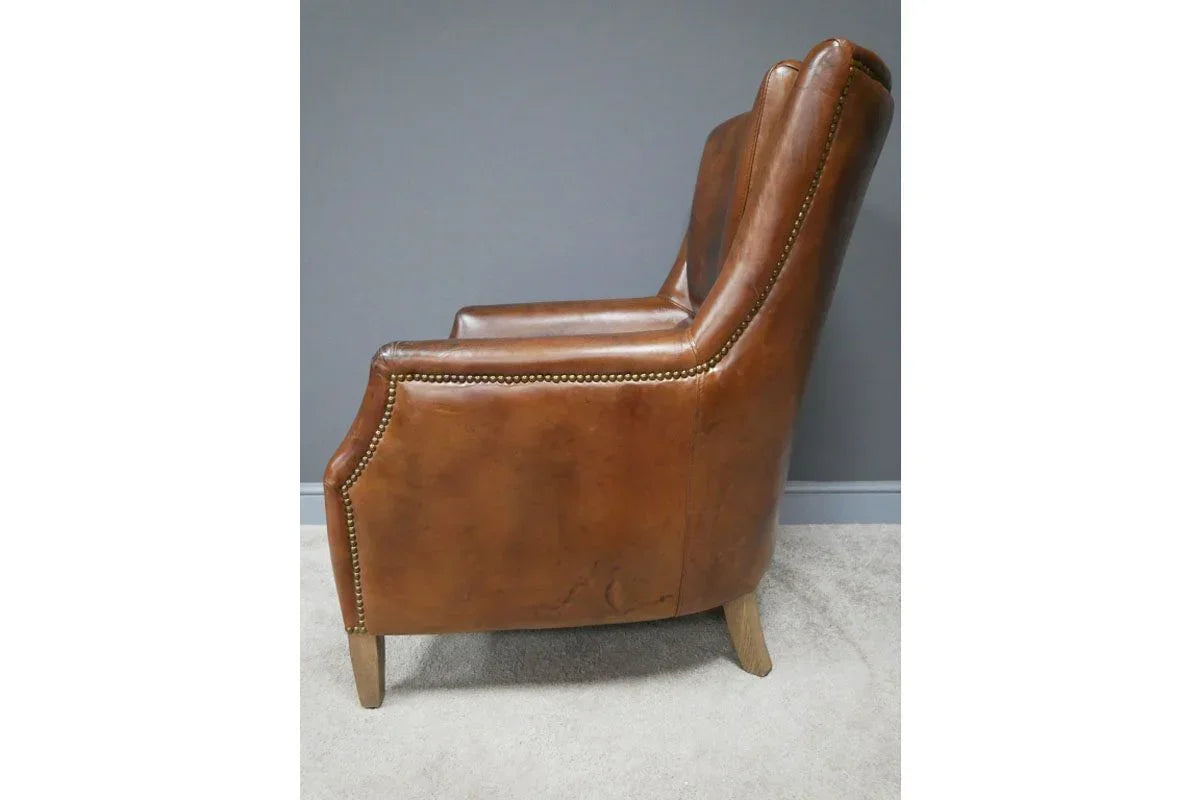 Side view of brown leather armchair with studded trim and wooden legs on beige carpet