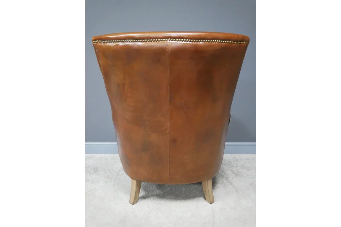 Back view of brown leather armchair with studded trim and wooden legs on carpet
