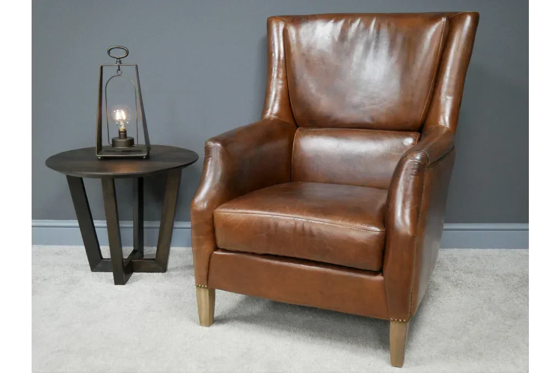 Brown leather armchair with high back beside round wooden side table and lamp