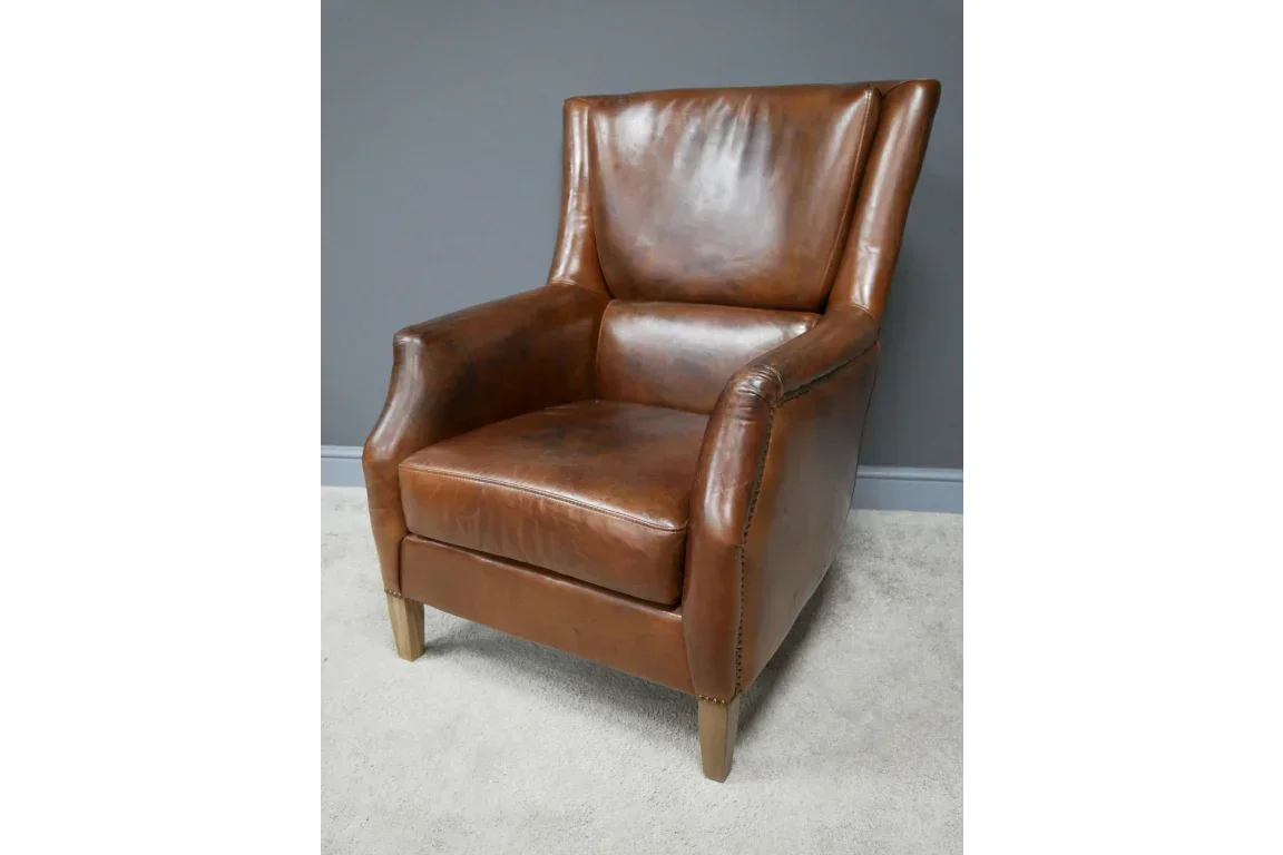 Brown leather armchair with wooden legs and high back on light carpet