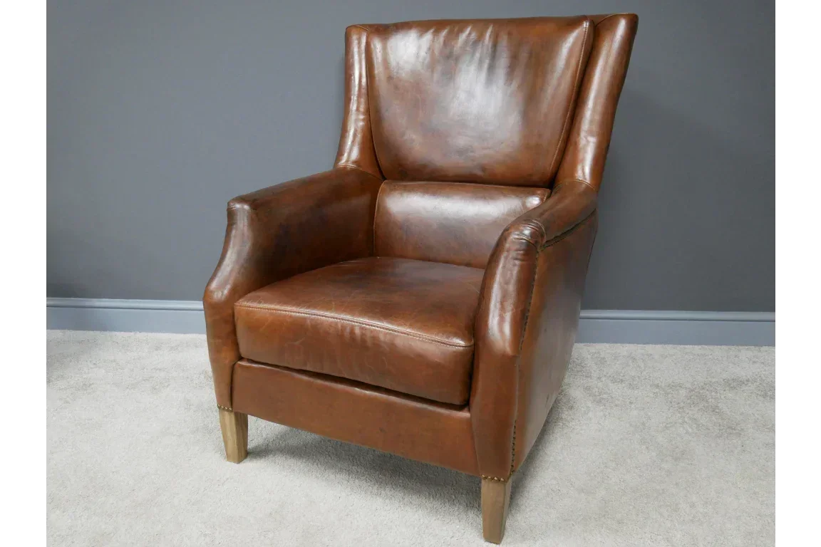 Brown leather armchair with high back and wooden legs on light carpet