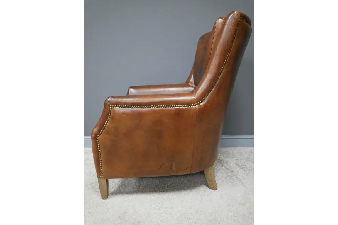 Side view of brown leather armchair with brass stud trim and wooden legs on carpet