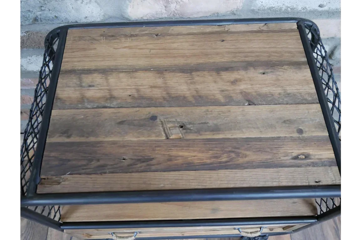 Industrial side table with rustic wood top and black metal mesh frame against brick wall