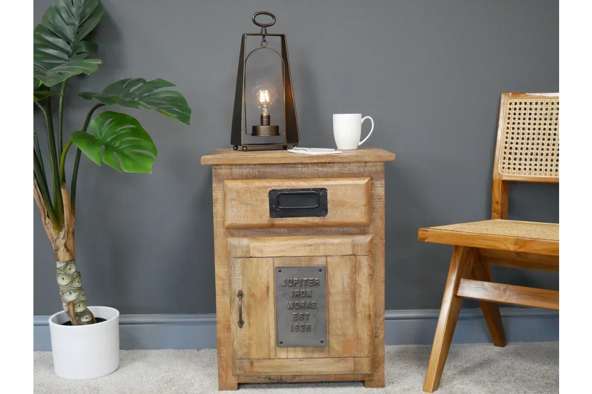 Rustic wood bedside table with metal handle, lamp and white mug, set against grey wall