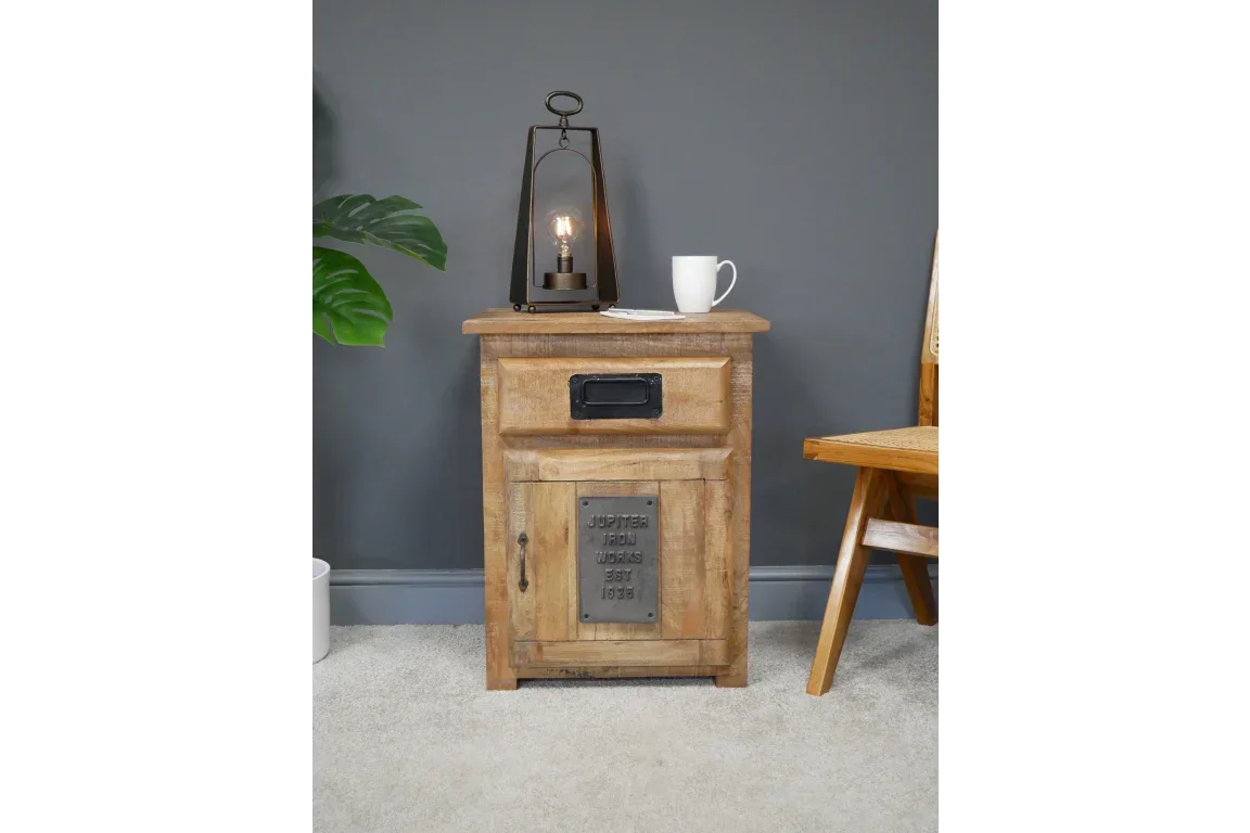 Rustic wooden bedside cabinet with drawer and door, lamp and mug on top, grey wall backdrop