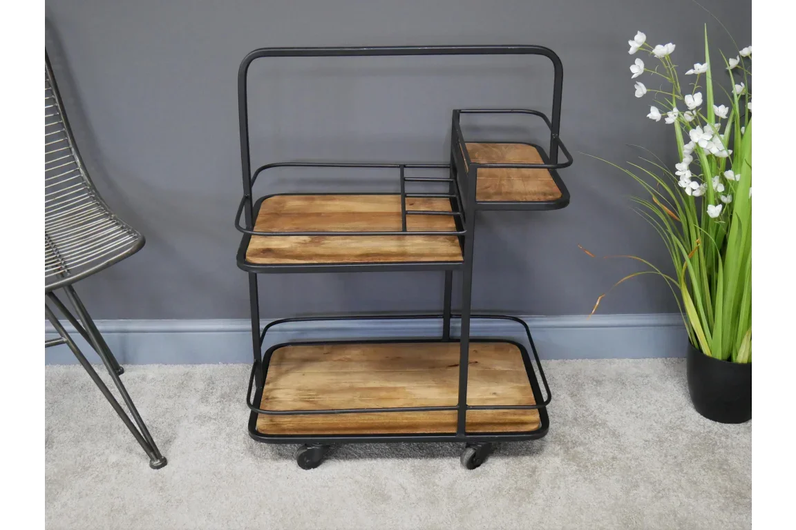 Industrial style metal and wood drinks trolley with shelves and wheels against grey wall