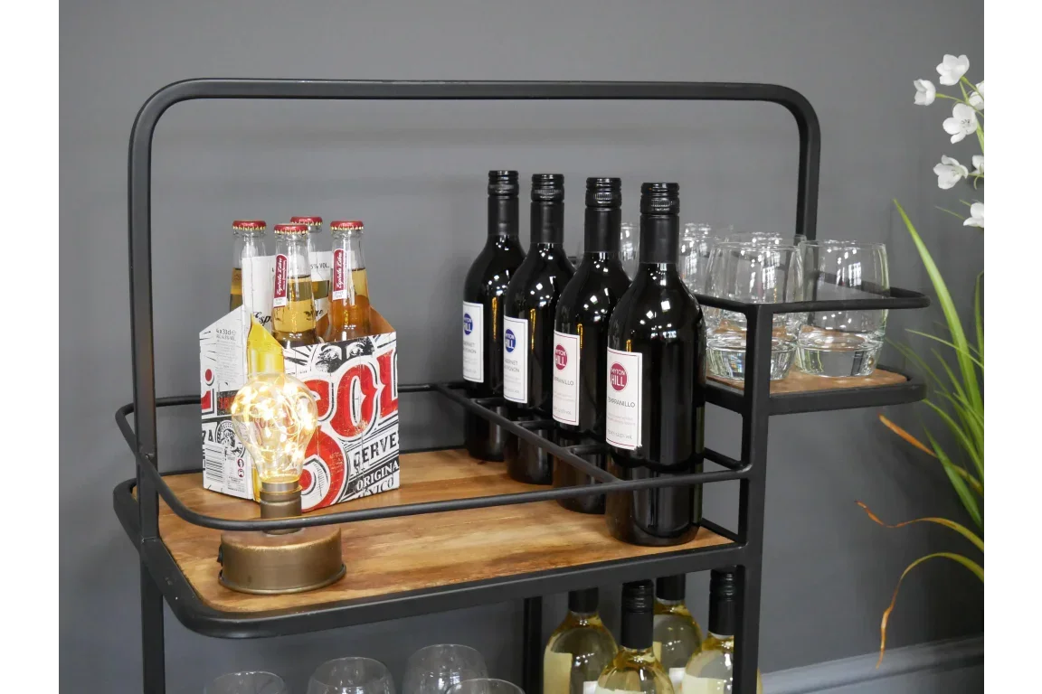 Industrial style bar cart with wooden shelves holding wine bottles, beer, glasses, light bulb