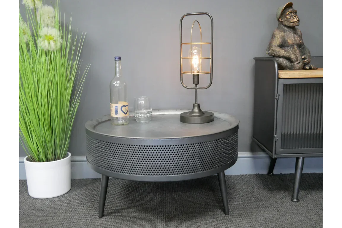 Round black metal coffee table with mesh sides, bottle, glass, and modern lamp on top