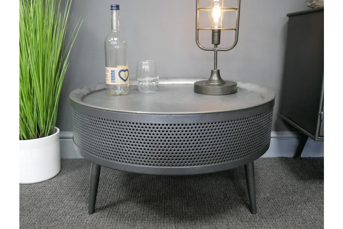 Round metal coffee table with perforated sides, bottle, glass, and lamp on top