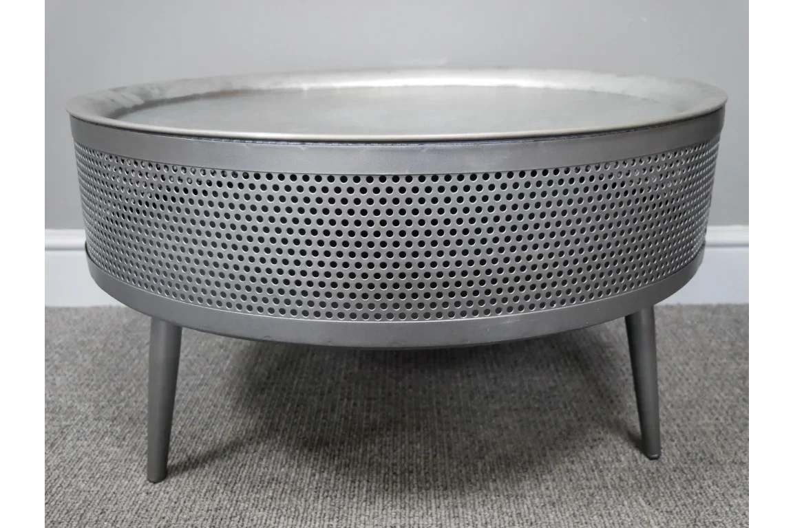 Round metal coffee table with perforated sides and three legs on grey carpet