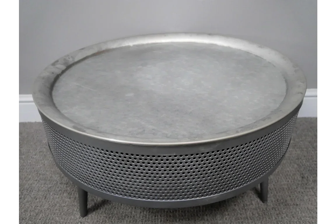 round metal coffee table with perforated steel frame and grey finish on carpeted floor