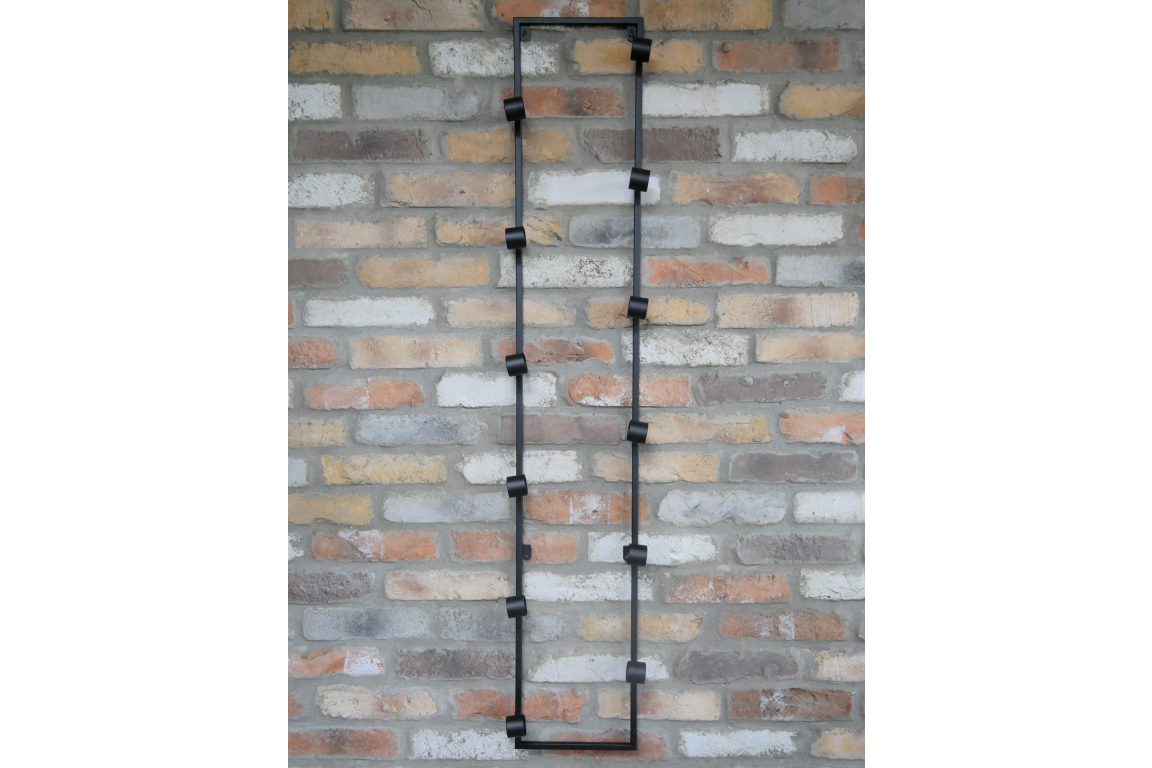Tall black metal wine bottle holder with multiple circular holders mounted vertically on a brick wall.