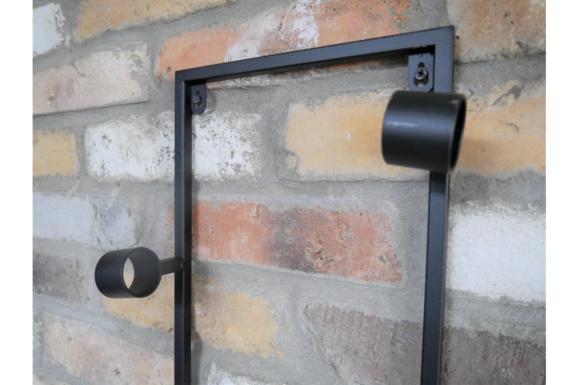 Black metal wine bottle holder mounted on a multicolored brick wall, side angle view.