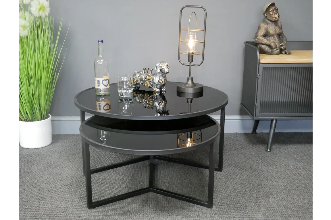 Black glass nesting coffee tables with modern lamp and decor in living room setting