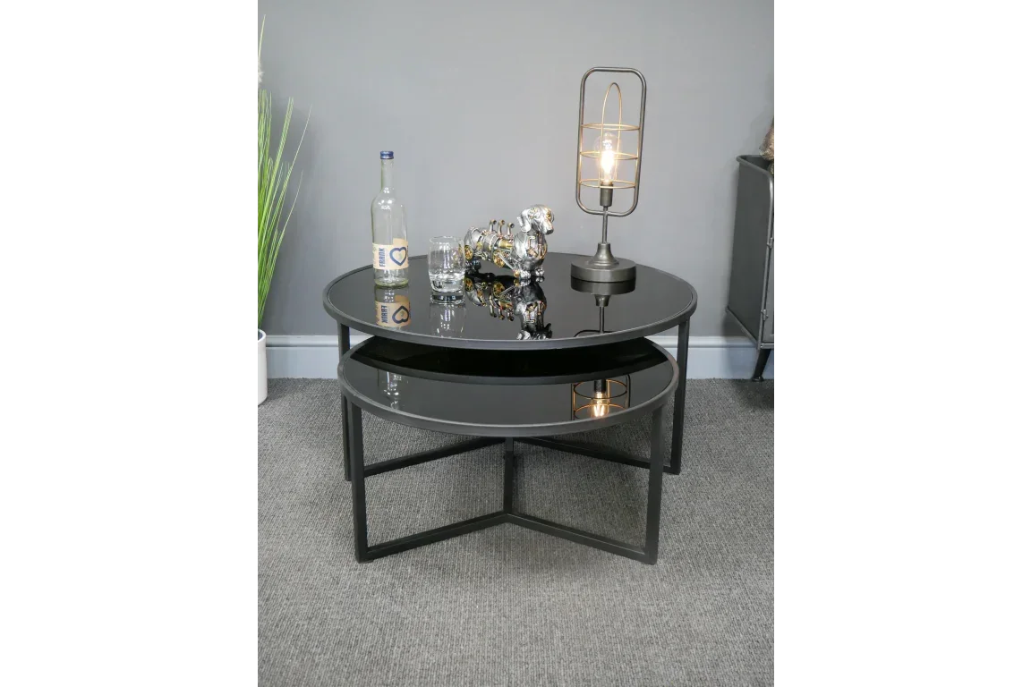 Black glass nesting coffee tables with metal frames styled with lamp, bottle, and decor