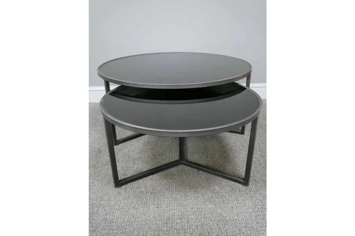Round black glass nesting coffee tables with metal frames on carpet