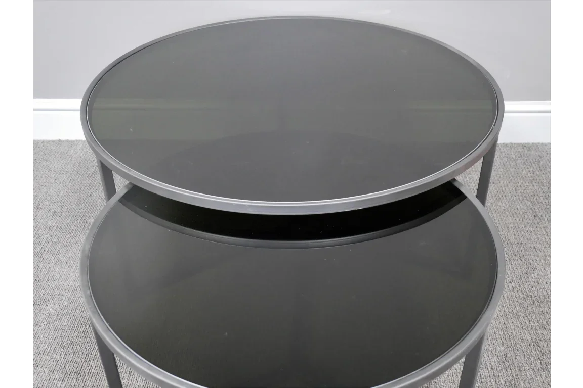 Round black glass coffee table with metal frame and lower shelf on grey carpet