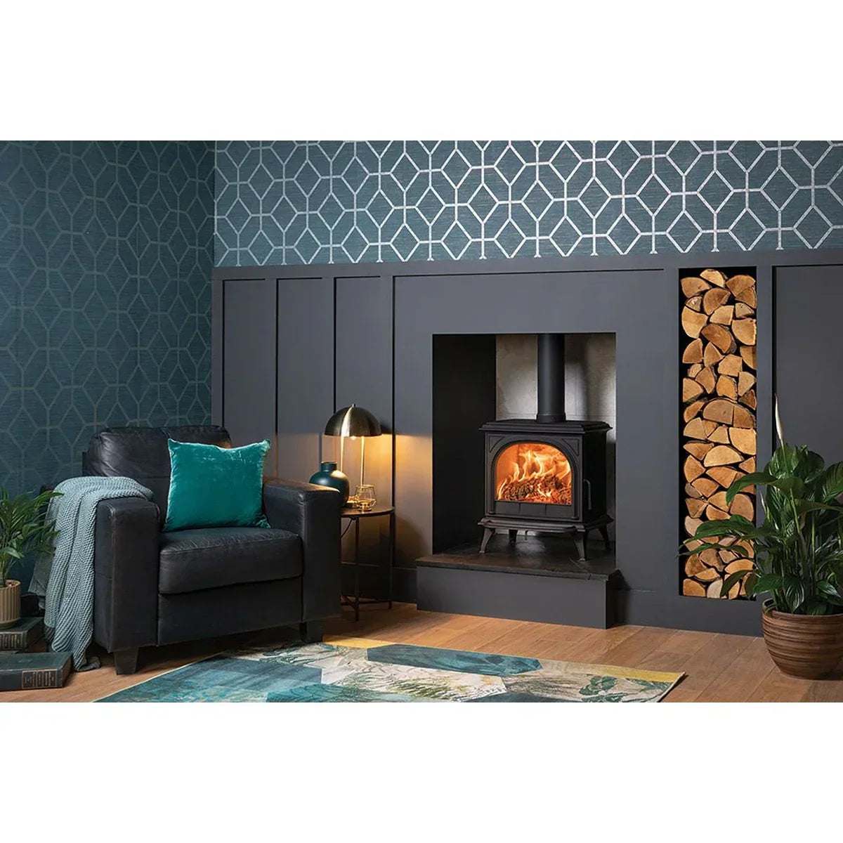 Living room with black leather armchair, teal pillow, wood burning stove and log storage